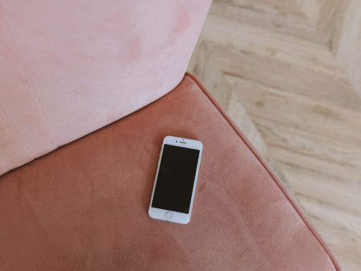 Minimalist composition of a smartphone on a pink couch corner, top view.