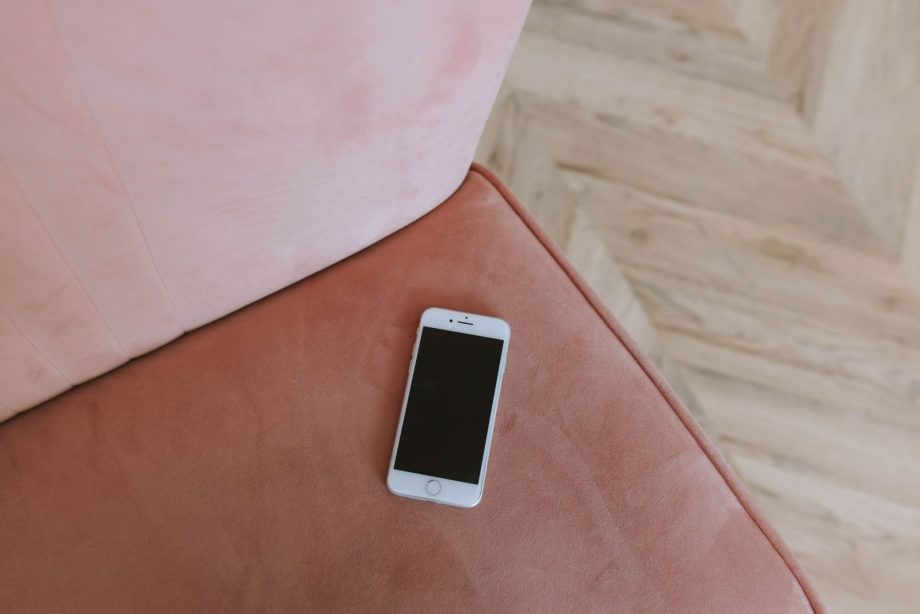 Minimalist composition of a smartphone on a pink couch corner, top view.
