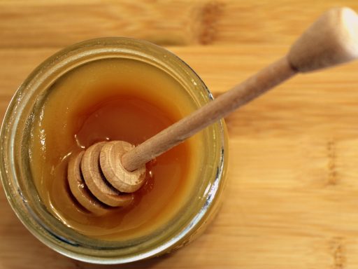 Een glazen pot honing met een houten lepel ernaast