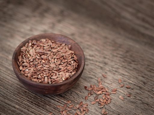 Een houten schaaltje gevuld met groene pompoenpitten op een houten tafelondergrond