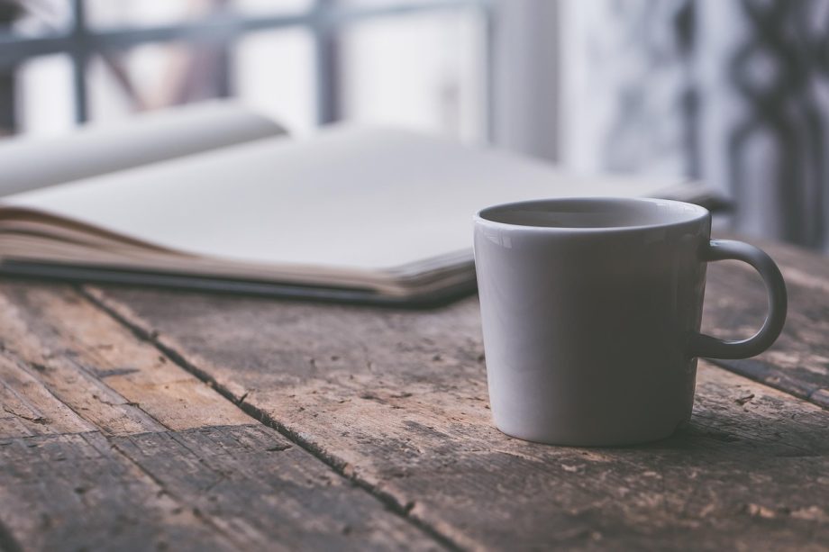 Persoon zit aan tafel en schrijft in een notitieboek, nadenkend over persoonlijk welzijn